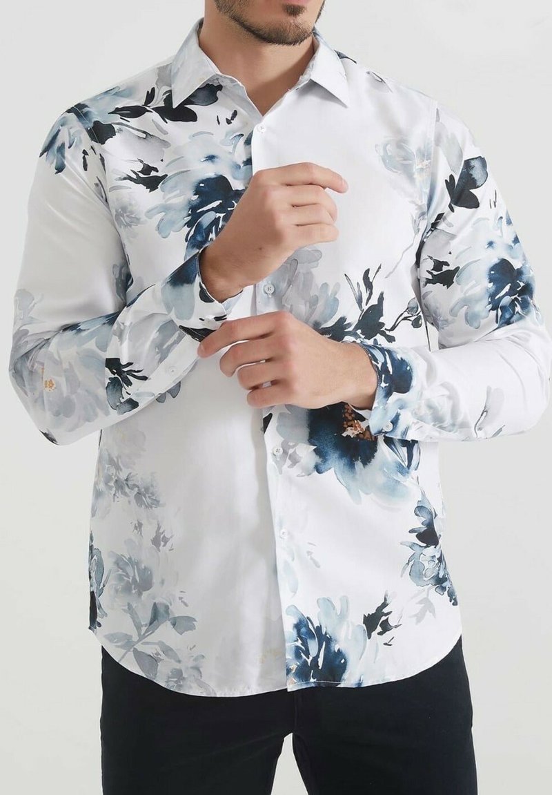 Chemise blanche avec un motif floral bleu, à boutons, à manches longues, texture lisse et accents bleus contrastants sur les poignets.