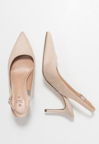 Chaussures à talons hauts en suède beige avec des orteils pointus et un design à bride arrière. Présente une délicate strap de cheville et un talon effilé.