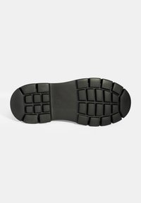 Semelle de chaussure en caoutchouc noire avec une surface texturée, présentant un motif en grille et des crampons rectangulaires pour l'adhérence et la durabilité.