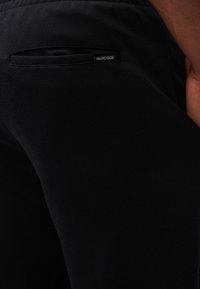 Black pants made of textured fabric with a side pocket. Features a small INDICODE label attached near the pocket.