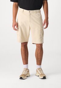 Beige cargo šortky se dvěma bočními kapsami, vyrobené z bavlny, se standardním střihem a zapínáním na knoflík v pase, doplněné béžovými sportovními botami.