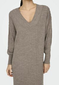 Abito a maglia rigata marrone con scollo a V e maniche lunghe a palloncino. La texture è morbida e il design è aderente con un taglio sopra il ginocchio.