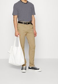 Maglietta a strisce blu navy e bianca, pantaloni beige, cintura nera, sneakers nere e una borsa a spalla bianca in tela. Outfit casual con colori a contrasto.