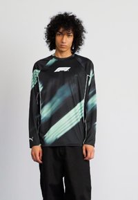 Zwarte langemouwen shirt met groene diagonale strepen, met een wit logo aan de voorkant. Gemaakt van een soepele stof met een relaxte pasvorm.