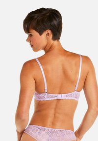 Soutien-gorge en dentelle lavande avec bretelles réglables et un fermoir décoratif au dos ; présente des motifs floraux complexes et des bords festonnés.