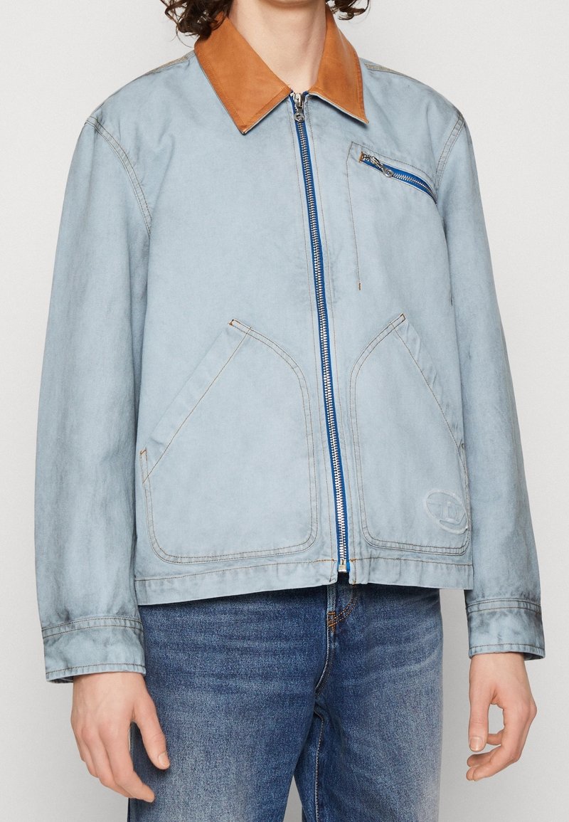 Ljusblå denimjacka med brunt läderkrage, frontdragkedja, två sidofickor och en liten bröstficka med blå dragkedja.