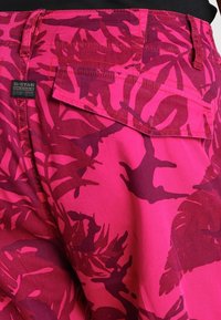 Rosa shorts med ett djärvt, mörkrosa tropiskt bladmönster, med en bakficka och kontrasterande sömmar. Märkesskylt synlig på midjan.