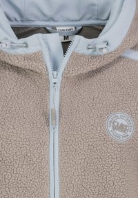Beige fleece jack met lichtblauwe accenten, een ritssluiting aan de voorkant en een logo patch. Zachte textuur met een capuchon en een ontspannen pasvorm.