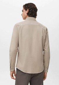 Camisa beige de manga larga con puños de botón y un cuello estructurado, que presenta una textura suave y un dobladillo curvado en la parte posterior.