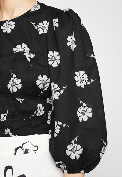 Blusa floral preta com padrões de flores brancas, com mangas bufantes e detalhe de cintura franzida, confeccionada em tecido leve.