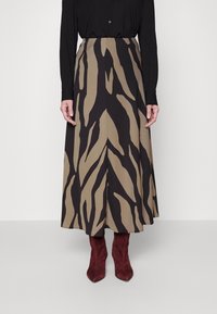 Ein locker sitzender Midirock mit einem Zebramuster in Beige und Schwarz, aus einem weichen Stoff gefertigt, kombiniert mit burgunderfarbenen Wildlederstiefeln.