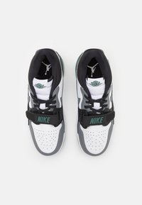 Nike tenisice u bijeloj i sivoj boji, s crnim akcentima, perforiranim gornjim dijelom i trakama s "NIKE" natpisom. Prikazan Jordan logo.