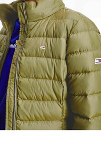 Olivgrön puffjacka med dragkedja fram, tryckknappskrage och horisontell quiltning. Har logopatchar på bröstet och ärmen.