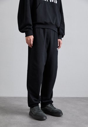 Schwarze Sweatpants aus weichem Stoff, mit elastischem Bund und seitlichen Nähten. Kombiniert mit schwarzen, strukturierten Schnürschuhen.
