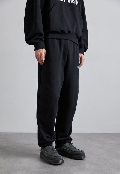 Pantaloni sportivi neri realizzati in tessuto morbido, con vita elastica e cuciture laterali. Abbinati a scarpe nere in tessuto intrecciato con lacci.