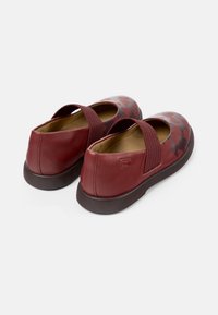 Scarpe in pelle rossa con un design testurizzato che presenta un motivo di cuori scuri, fasce elastiche sulla parte superiore e una suola piatta marrone.