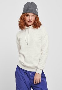 Vaalean beige huppari, jossa on naru, ribbaattiset hihansuut ja rento malli, yhdessä sinisten cargo-shortsien ja harmaan ribbaatin beanie-pipon kanssa.