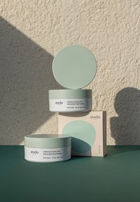 Due contenitori rotondi con coperchi verde menta, etichettati "Patch per gli occhi antiossidanti alla caffeina e tè verde", accanto a una scatola con un motivo coordinato.