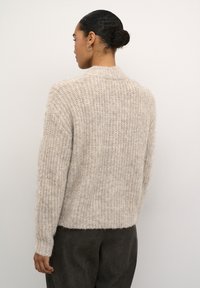 Beige gebreide trui met een textuurafwerking, ronde halslijn en lange mouwen. De achterkant heeft een traditionele snit met minimale details.