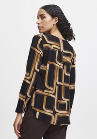 Blusa a maniche lunghe nera con un motivo geometrico dorato. Caratterizzata da una vestibilità ampia, scollo rotondo e polsini con bottone. Tessuto dalla texture liscia.