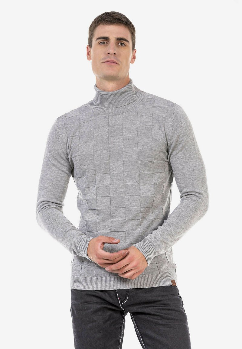 Grijze coltrui met een gestructureerd vierkant patroon. Geribbelde boorden en zoom. Model staat met handen samengevouwen, draagt donkere jeans.