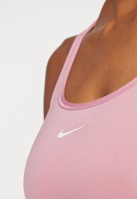 Roza sportska majica bez rukava s okruglim izrezom, s bijelim Nike logotipom sprijeda. Glatka tkanina s minimalnim detaljima šivanja.