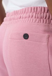 Roze sweatpants met een gathered tailleband en een enkele achterzak met een zwarte knoop. Zachte textuur, eenvoudig ontwerp en geen patronen.