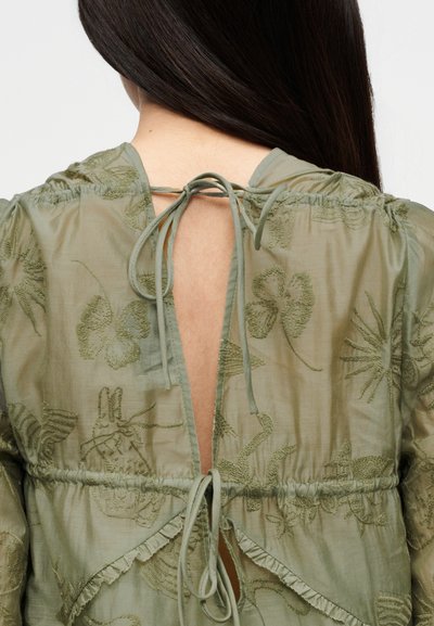 Ανοιχτοπράσινη κεντητή μπλούζα με χαμηλή πλάτη και κλείσιμο με κορδόνι, με σούρες στη μέση και λουλουδένια σχέδια σε σκούρο πράσινο νήμα.