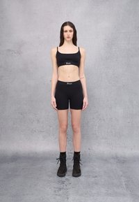 Top corto negro y pantalones cortos ajustados, hechos de tela elástica; cuenta con un logo en la cintura, combinado con botas negras de cordones.