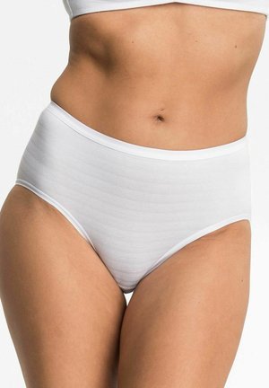 Frau in weißen hochgeschnittenen Unterhosen und passendem kurz geschnittenen Oberteil, das den Bauch und die Oberschenkel zeigt, vor einem einfarbigen Hintergrund.