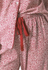 Roter Pyjama-Set mit floralem Muster aus weichem Stoff. Verfügt über ein Hemd mit Knopfleiste und einen elastischen Bund mit einer passenden roten Schleife.
