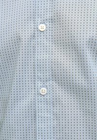 Camicia azzurra chiara con piccoli motivi floreali scuri. Presenta una chiusura con bottoni, un tessuto testurizzato e un classico design del colletto.