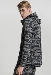 Sudadera con capucha de camuflaje gris, con cierre zip y cuello alto. Presenta mangas largas, tejido texturizado y un ajuste ceñido.