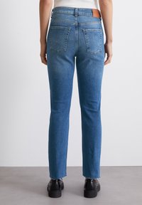 Jeans de mezclilla azul con un diseño de pierna recta, que cuentan con bolsillos traseros, una cintura alta y dobladillos deshilachados. Parche de cuero marrón en la cinturilla.