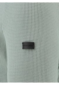 Waffelstrick-Minzpullover mit einem schwarzen Stofflabel mit dem Text "KEY LARGO". Strukturierten, gerippten Oberfläche und langen Ärmeln.
