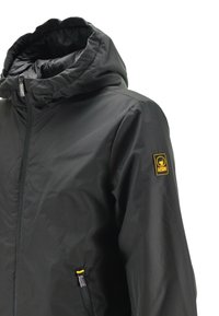 Giacca nera con cappuccio, chiusura frontale con zipper, tasca laterale con zipper e toppa con logo giallo sulla manica sinistra.