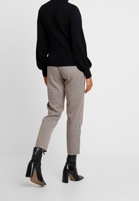 Černý svetr s objemnými rukávy, doplněný hnědými kostkovanými kalhotami. Černé kotníkové boty s masivním podpatkem dokončují outfit.