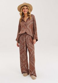 Hnedý vzorovaný domáci set obsahuje voľnú košeľu na gombíky a široké nohavice. Mäkkučký materiál s paisley vzormi. Okrúhla čiapka ako doplnok.