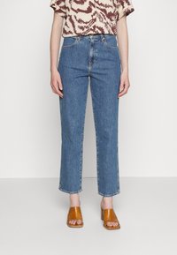 Blå raka jeans med hög midja, med en klassisk femficksdesign och kontrasterande sömmar, kombinerade med beige klacksandaler.