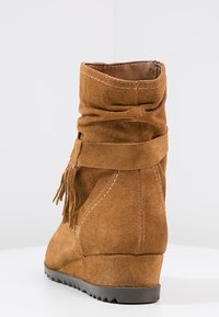 Bruine suède enkellaars met een slouchy ontwerp, decoratieve franjes en een wiggenhak. Heeft contrasterende stiksels en een gestructureerde zool.