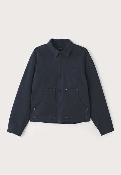 Navy blue jacket made of fabric, featuring a zip front, pointed collar, two large front pockets, and subtle logo embroidery.