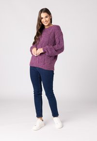 Lila gestrickter Pullover mit strukturiertem Design und Ballonärmeln, kombiniert mit dunkelblauen Skinny-Jeans und weißen Sneakers.