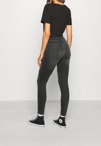 Camiseta negra combinada con jeans ajustados de cintura alta en gris oscuro y zapatillas altas negras con acentos blancos. Diseño simple y ajustado.