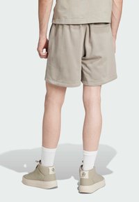 Lysebeige shorts lavet af blødt materiale med elastisk talje og sidelommer, parret med lysebeige høj-top sneakers og hvide sokker.