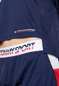 Námořnická síťovaná krátkosrstá halenka s logem "TOMMY SPORT" v červené a bílé barvě; elastický pas má logo v podobných barvách.