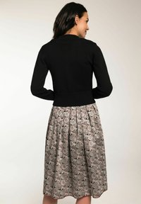 Schwarze Strickjacke mit Rippenabschluss, kombiniert mit einem knielangen, floralen Rock mit einem grau-pinken Muster und Faltenlegung.