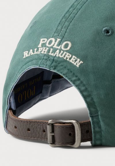 Zaļš kokvilnas cepure ar baltu uzrakstu "Polo Ralph Lauren" reljefā. Tam ir brūna ādas siksna ar metāla sprādzi un rūtainas raksta iekšējā oderējuma.