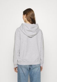 Felpa grigia con una consistenza morbida, caratterizzata da un ampio cappuccio e polsini a coste. Abbinata a jeans azzurri chiari.