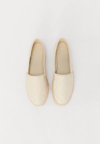 Beige nazouvací boty s embosovaným vzorem a tkanou juty jako podešev. Zaoblená špička a měkký vrchní materiál. Logo značky viditelné na stélce.