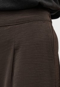 Κοντινό πλάνο τσέπης και μέσης παντελονιού από σκούρο καφέ ύφασμα με ορατή ραφή και μαλακό, υφασματικό υλικό.